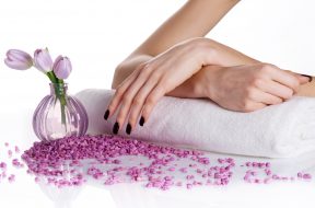 Spa manicure treatment: woman hands with dark manicure lying down on a white terry towel