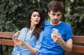 Young couple in the park. Boy is checking his phone hiding it. Girl is lookin into boyfriend's phone with mistrust. What is in your phone concept