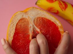 Fingers in grapefruit on pink background. Composition with fresh banana with traces of red lipstick and grapefruit on pink background.