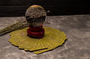 Forecasting, fortune telling, occult concept. Cartomancy, occult science. Crystal ball and tarot cards on grey background. Magic tarot cards spread on a table surrounding crystal ball for magic ritual