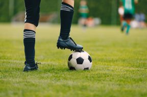 One young football player with ball on grass field. Boy in a sportswear. Player wearing black football socks and soccer cleats. Football horizontal closeup background