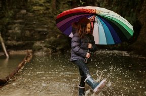 Happy girl playing by the forest lake with an umbrella on a rainy day