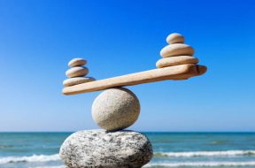 Symbolic scales of stones on the background of the sea and blue sky. Concept of harmony and balance. Pros and cons concept