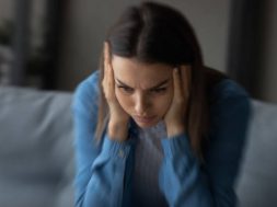 Close up unhappy woman suffering from strong headache and dizziness, depressed young female blurry motion background, sitting on couch alone, touching temples, feeling pain, unwell and unhealthy