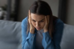 Close up unhappy woman suffering from strong headache and dizziness, depressed young female blurry motion background, sitting on couch alone, touching temples, feeling pain, unwell and unhealthy