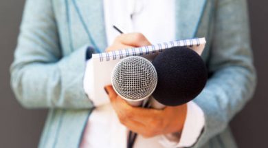 Female reporter at press conference, writing notes, holding microphone
