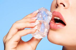 Closeup portrait of beautiful young woman applies the ice to face on a blue background.