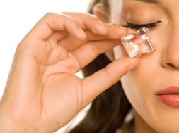 young beautiful woman holding ice cube under the eye on white background
