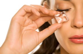 young beautiful woman holding ice cube under the eye on white background