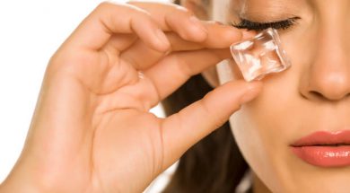 young beautiful woman holding ice cube under the eye on white background