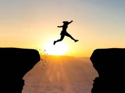 Woman jumping over abyss in fornt of sunset.