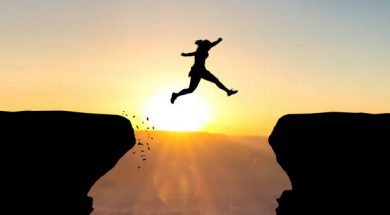 Woman jumping over abyss in fornt of sunset.