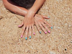 Unrecognizable woman hands with pink and blue manicure nails on sandy beach background