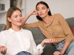 Jealous Woman Listening With Envy To Her Friend Bragging About Great Life Sitting On Sofa In Modern Living Room At Home. Envious Lousy Friends, Fake Friendship Concept. Selective Focus